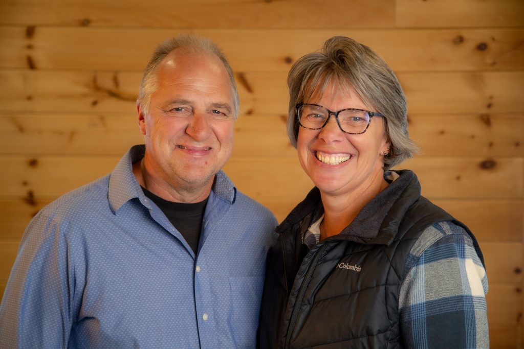 Inge and Henry (Jr.) Koskamp standing together indoors against a wooden wall